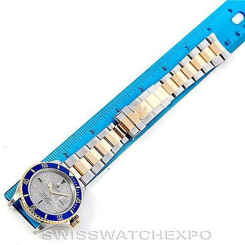 The Rolex Submariner 16613 Men's Steel and Gold (two tone) Grey Dial 16613 Men's Steel and Gold (two tone) Grey Dial watch is shown from a top-down angle next to a ruler, displaying the entire bracelet and face.