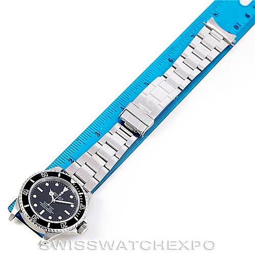 The Rolex Submariner 14060 Men
s Stainless Steel Black Dial 14060 Men
s Stainless Steel Black Dial watch is displayed flat, showing the full face and band against a blue ruler for scale.