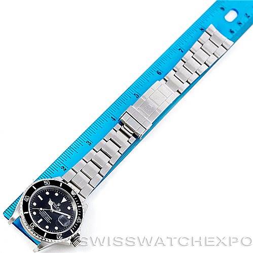 The image shows a Rolex Submariner 16610 Men
s Stainless Steel Black Dial 16610 Men
s Stainless Steel Black Dial watch laid flat next to a blue ruler, displaying the entire bracelet and bezel from a top-down angle.