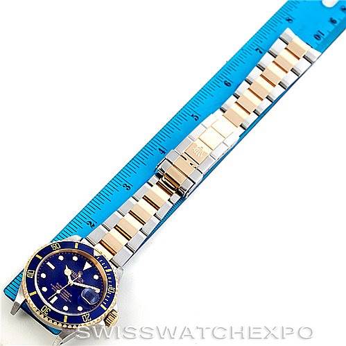 The image shows a Rolex Submariner 16613 Men's Steel and Gold (two tone) Blue Dial 16613 Men's Steel and Gold (two tone) Blue Dial watch laid flat, with a focus on its face, bezel, and bracelet against a measuring ruler.