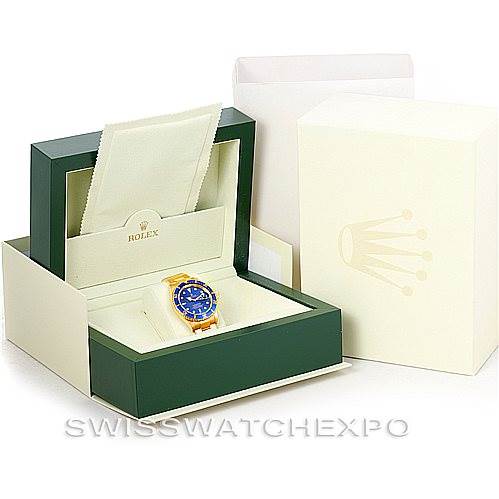 The image shows a Rolex Submariner 16618 Men's Yellow Gold Blue Dial 16618 Men's Yellow Gold Blue Dial watch inside its box, along with a cleaning cloth and outer packaging, viewed from an angle above the watch.