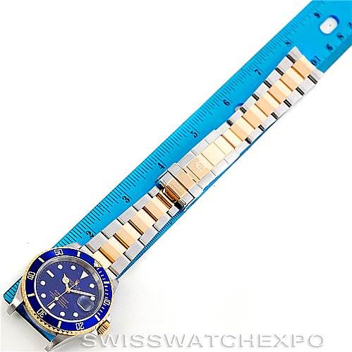 The Rolex Submariner 16613 Men's Steel and Gold (two tone) Blue Dial 16613 Men's Steel and Gold (two tone) Blue Dial watch is shown fully extended next to a blue ruler, displaying the face and bracelet.