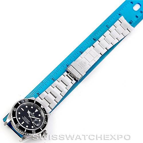 The image shows a Rolex Submariner 16610 Men's Stainless Steel Black Dial 16610 Men's Stainless Steel Black Dial watch laid flat with its strap extended alongside a blue ruler.