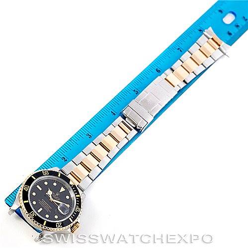 The Rolex Submariner 16613 Men
s Steel and Gold (two tone) Black Dial 16613 Men
s Steel and Gold (two tone) Black Dial watch is shown from an overhead angle, with its bracelet aligned alongside a blue measuring ruler.