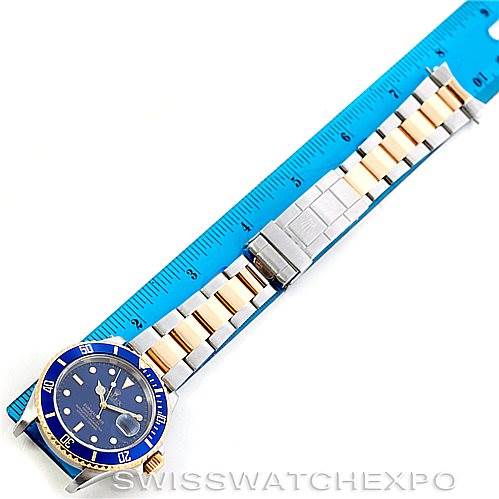 This image shows a top-down view of a Rolex Submariner 16613 Men's Steel and Gold (two tone) Blue Dial 16613 Men's Steel and Gold (two tone) Blue Dial watch with a blue dial and a two-tone bracelet next to a blue ruler.