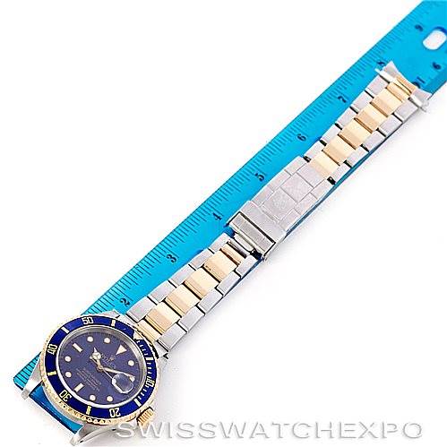 The image shows a Rolex Submariner 16613 Men
s Steel and Gold (two tone) Blue Dial 16613 Men
s Steel and Gold (two tone) Blue Dial watch from a top view, displaying the face, bezel, and full bracelet next to a ruler for scale.