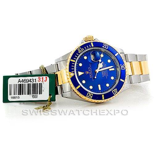 This image shows a Rolex Submariner 16613 Men
s Steel and Gold (two tone) Blue Dial 16613 Men
s Steel and Gold (two tone) Blue Dial watch with a blue dial, gold bezel, and two-tone bracelet from a front angle, along with its tags.