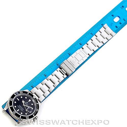 The image shows a Rolex Submariner 16610 Men's Stainless Steel Black Dial 16610 Men's Stainless Steel Black Dial watch with a stainless steel bracelet, placed next to a blue ruler for scale.