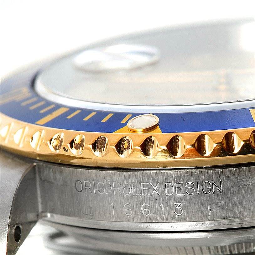 This close-up of a Rolex Submariner 16613 Men's Steel and Gold (two tone) Champagne Dial 16613 Men's Steel and Gold (two tone) Champagne Dial shows the bezel, part of the dial, and the engraved model number 16613.