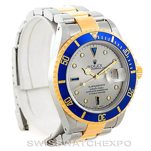 The image shows a Rolex Submariner 16613 Men's Steel and Gold (two tone) Grey Dial 16613 Men's Steel and Gold (two tone) Grey Dial watch with a silver dial, blue and gold bezel, and a silver and gold bracelet, viewed from the front-left angle.