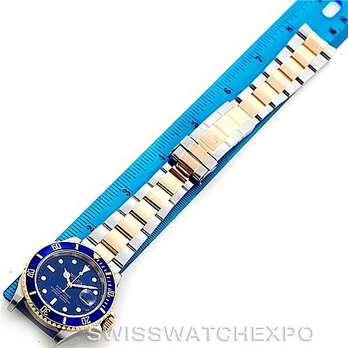 This image shows a Rolex Submariner 16613 Men
s Steel and Gold (two tone) Blue Dial 16613 Men
s Steel and Gold (two tone) Blue Dial watch laid flat with its bracelet fully extended alongside a blue ruler.