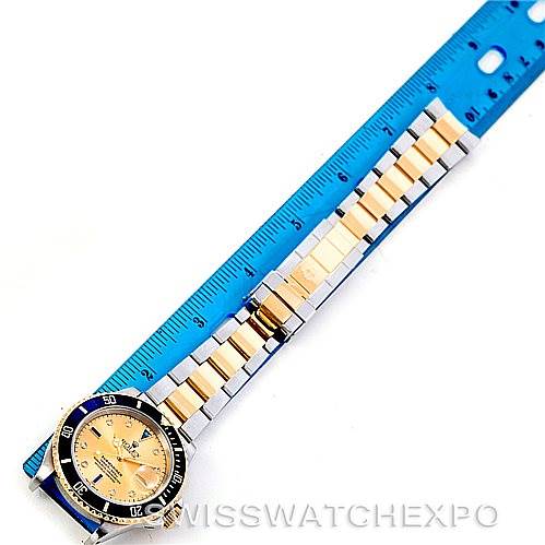 The image shows a Rolex Submariner 16613 Men's Steel and Gold (two tone) Champagne Dial 16613 Men's Steel and Gold (two tone) Champagne Dial watch laid flat alongside a ruler, displaying its strap and face diagonally.