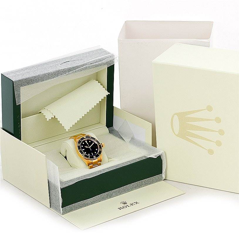 The image shows a Rolex Submariner 16618 Men
s Yellow Gold Black Dial 16618 Men
s Yellow Gold Black Dial watch in its packaging, including the watch box, outer box, and a cleaning cloth.