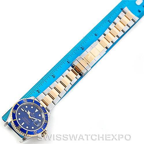 This top-down view shows the Rolex Submariner 16613 Men's Steel and Gold (two tone) Blue Dial 16613 Men's Steel and Gold (two tone) Blue Dial watch with a blue dial and bezel, alongside its metal bracelet against a blue ruler.