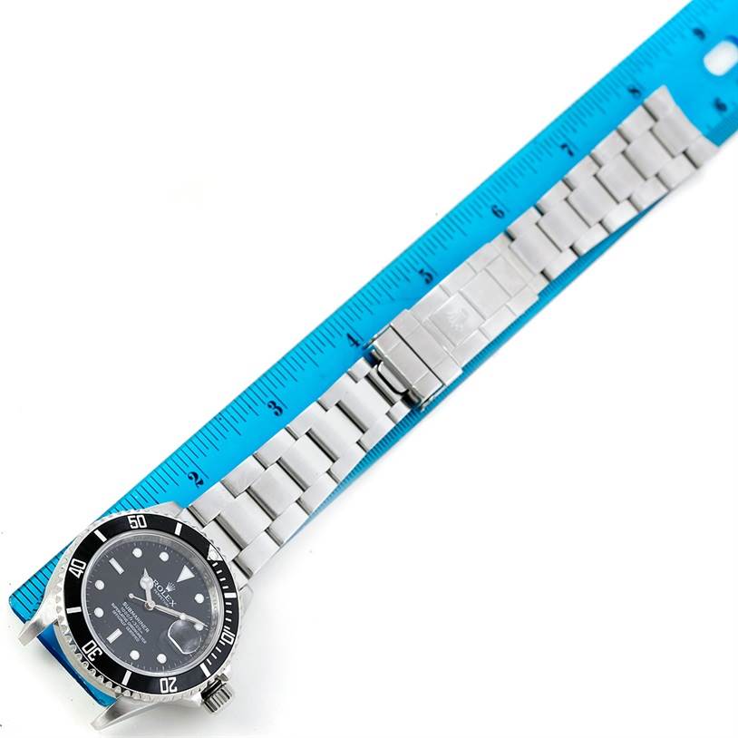 This top-down image shows the face and bracelet of a Rolex Submariner 16610 Men
s Stainless Steel Black Dial 16610 Men
s Stainless Steel Black Dial watch aligned with a ruler.