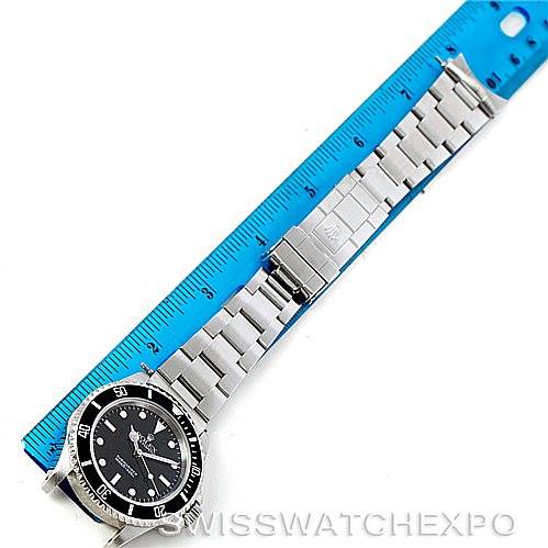 The image shows a Rolex Submariner 14060 Men
s Stainless Steel Black Dial 14060 Men
s Stainless Steel Black Dial watch laid flat with its band fully extended alongside a blue ruler.