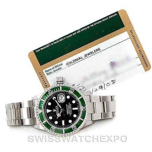 The image shows a front view of a Rolex Submariner 16610V Men
s Stainless Steel Black Dial 16610V Men
s Stainless Steel Black Dial watch with a green bezel and accompanying warranty card.