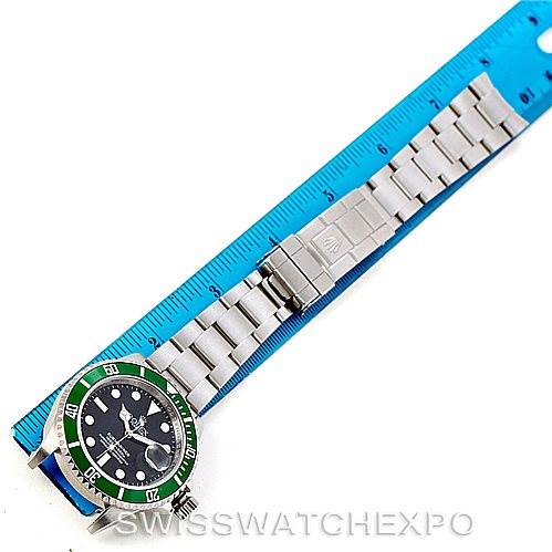 This image shows a top view of a Rolex Submariner 16610V Men
s Stainless Steel Black Dial 16610V Men
s Stainless Steel Black Dial watch with its full bracelet laid alongside a blue ruler.