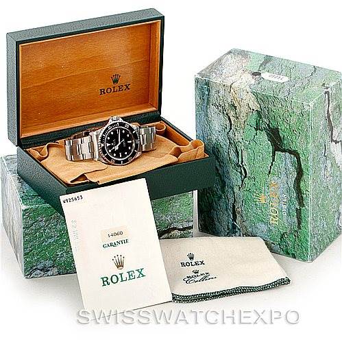 The image shows a Rolex Submariner 14060 Men
s Stainless Steel Black Dial 14060 Men
s Stainless Steel Black Dial model watch with its original packaging, including the box, guarantee card, and cleaning cloth.