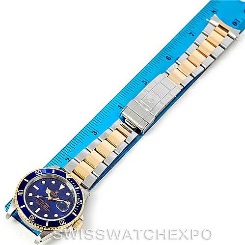 The image shows a top view of a Rolex Submariner 16613 Men's Steel and Gold (two tone) Blue Dial 16613 Men's Steel and Gold (two tone) Blue Dial watch with a gold and silver bracelet placed next to a ruler.
