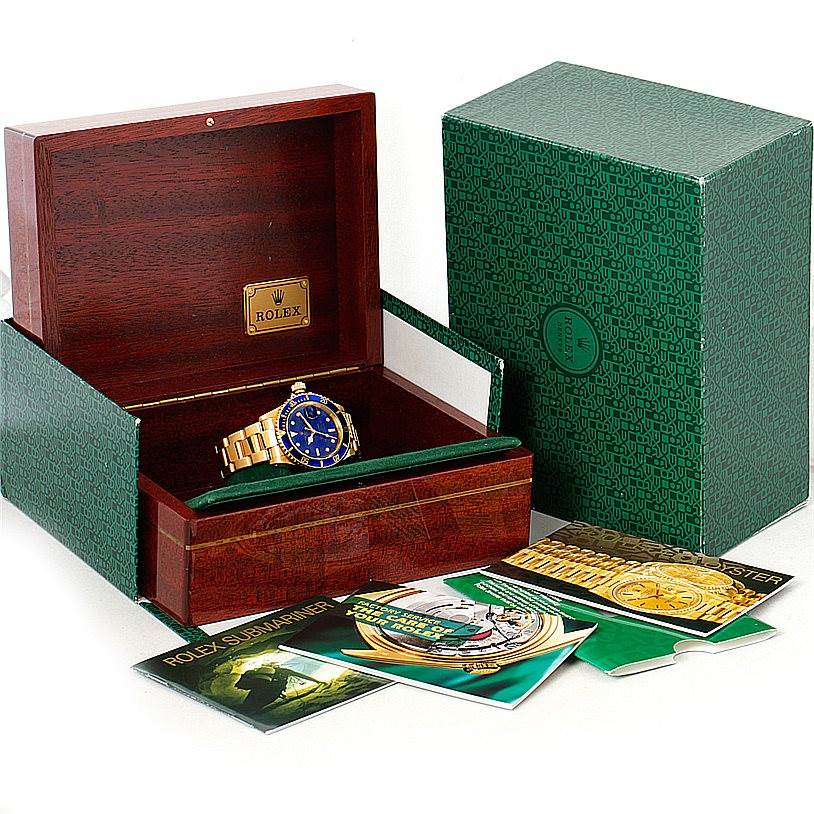 The Rolex Submariner 16618 Men
s Yellow Gold Blue Dial 16618 Men
s Yellow Gold Blue Dial watch is shown in its open wooden box, with the outer green box and booklets displayed around it.