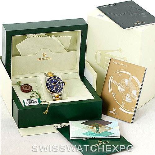This image shows a Rolex Submariner 16613 Men
s Steel and Gold (two tone) Blue Dial 16613 Men
s Steel and Gold (two tone) Blue Dial watch at an angle inside its green box along with accessories like booklets, a tag, and a cleaning cloth.