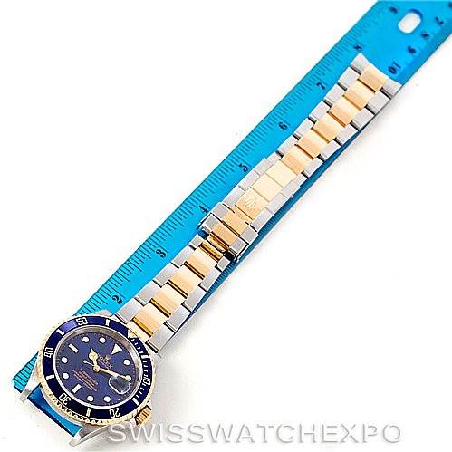This image shows a Rolex Submariner 16613 Men
s Steel and Gold (two tone) Blue Dial 16613 Men
s Steel and Gold (two tone) Blue Dial watch laid flat next to a blue ruler, displaying the face and band.