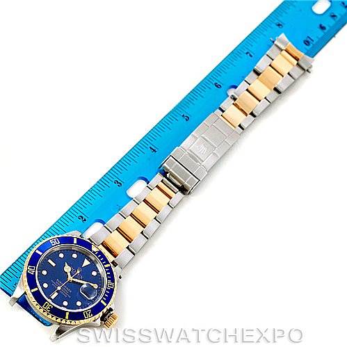 The image shows a Rolex Submariner 16613 Men's Steel and Gold (two tone) Blue Dial 16613 Men's Steel and Gold (two tone) Blue Dial watch from a top view, highlighting its blue dial, bezel, and two-tone bracelet alongside a blue ruler.