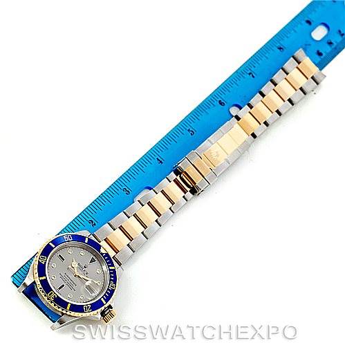 The image shows a top-down view of a Rolex Submariner 16613 Men's Steel and Gold (two tone) Grey Dial 16613 Men's Steel and Gold (two tone) Grey Dial watch with a two-tone bracelet and a blue bezel next to a ruler.