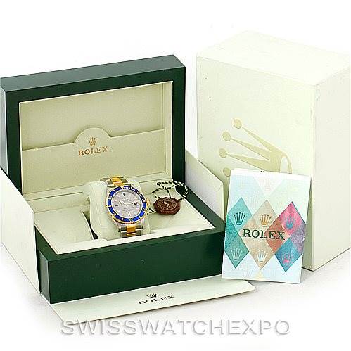 The image shows a Rolex Submariner 16613 Men's Steel and Gold (two tone) Grey Dial 16613 Men's Steel and Gold (two tone) Grey Dial watch at an angle, inside its display box, also with its outer box and warranty card.