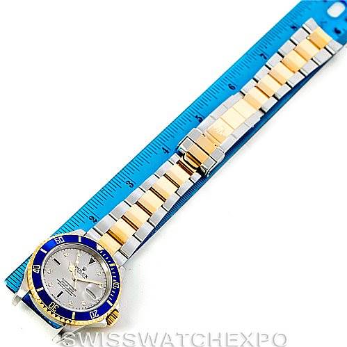 The image shows a top-down view of a Rolex Submariner 16613 Men
s Steel and Gold (two tone) Grey Dial 16613 Men
s Steel and Gold (two tone) Grey Dial watch, displaying its two-tone bracelet alongside a blue measuring ruler.