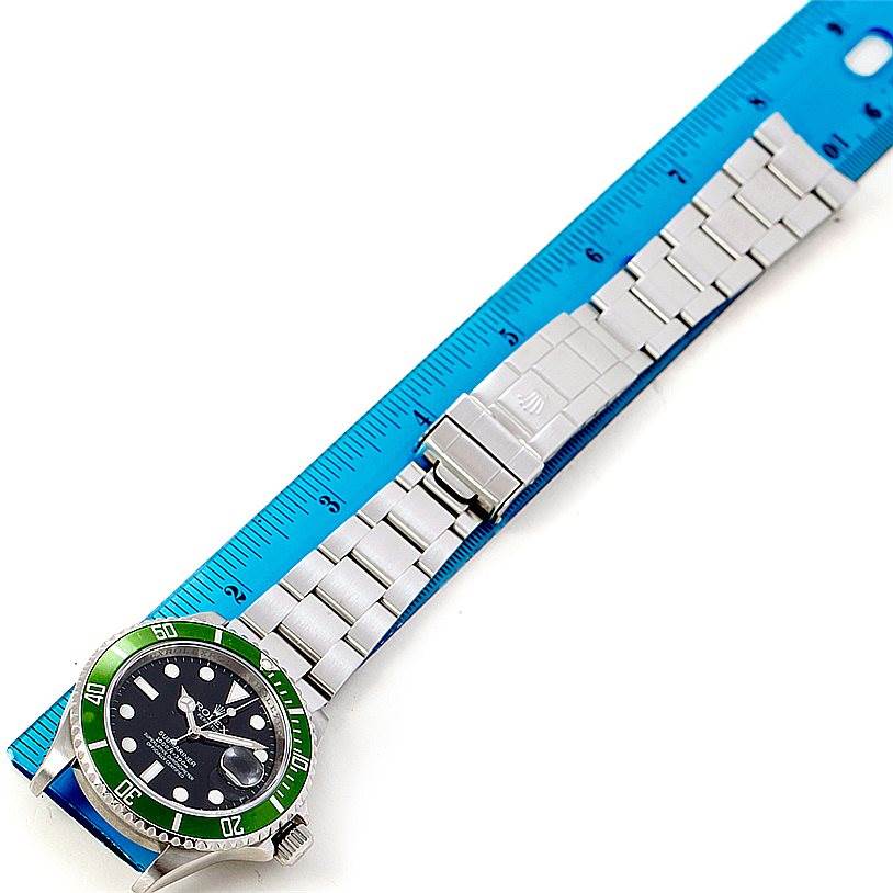 The image shows a Rolex Submariner 16610V Men
s Stainless Steel Black Dial 16610V Men
s Stainless Steel Black Dial watch laid flat next to a blue ruler, displaying the face, bezel, bracelet, and clasp from a bird
s-eye view.