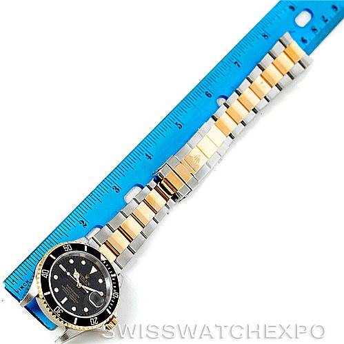 The image shows a top-down view of a Rolex Submariner 16613 Men's Steel and Gold (two tone) Black Dial 16613 Men's Steel and Gold (two tone) Black Dial watch with a two-tone bracelet, next to a blue ruler.