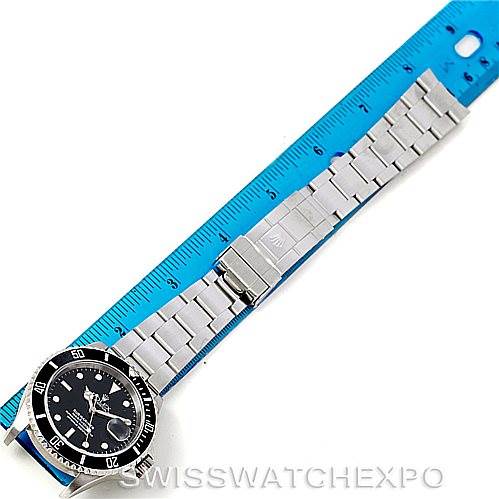 The Rolex Submariner 16610 Men
s Stainless Steel Black Dial 16610 Men
s Stainless Steel Black Dial watch is shown laid flat with a focus on its face, bracelet, and clasp alongside a ruler for scale.