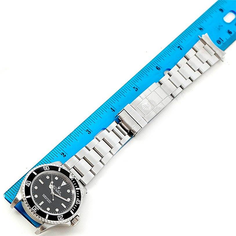 This image shows the Rolex Submariner 14060 Men
s Stainless Steel Black Dial 14060 Men
s Stainless Steel Black Dial watch laid flat next to a ruler, displaying its face and metal bracelet.