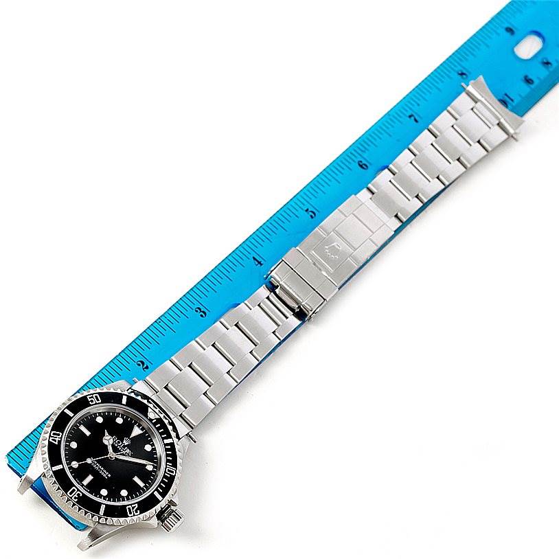 The image shows a top view of a Rolex Submariner 14060 Men
s Stainless Steel Black Dial 14060 Men
s Stainless Steel Black Dial watch with its stainless steel bracelet laid beside a blue ruler.