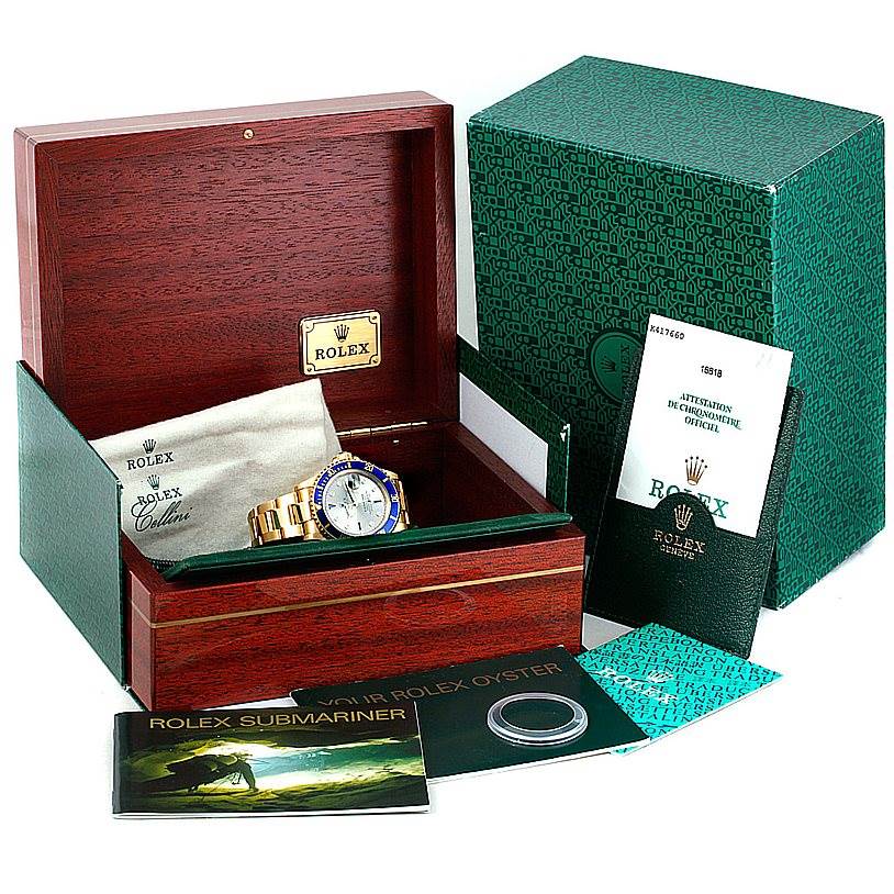 This image shows a Rolex Submariner 16618 Men's Yellow Gold Grey Dial 16618 Men's Yellow Gold Grey Dial watch in a wooden box with accessories like booklets and a green outer box.