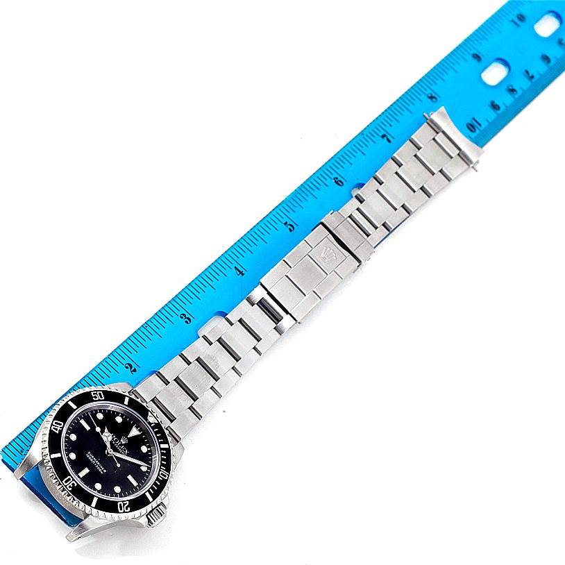 The image shows a Rolex Submariner 14060 Men
s Stainless Steel Black Dial 14060 Men
s Stainless Steel Black Dial watch from a top angle, displaying the dial, bezel, and bracelet beside a blue ruler for scale.