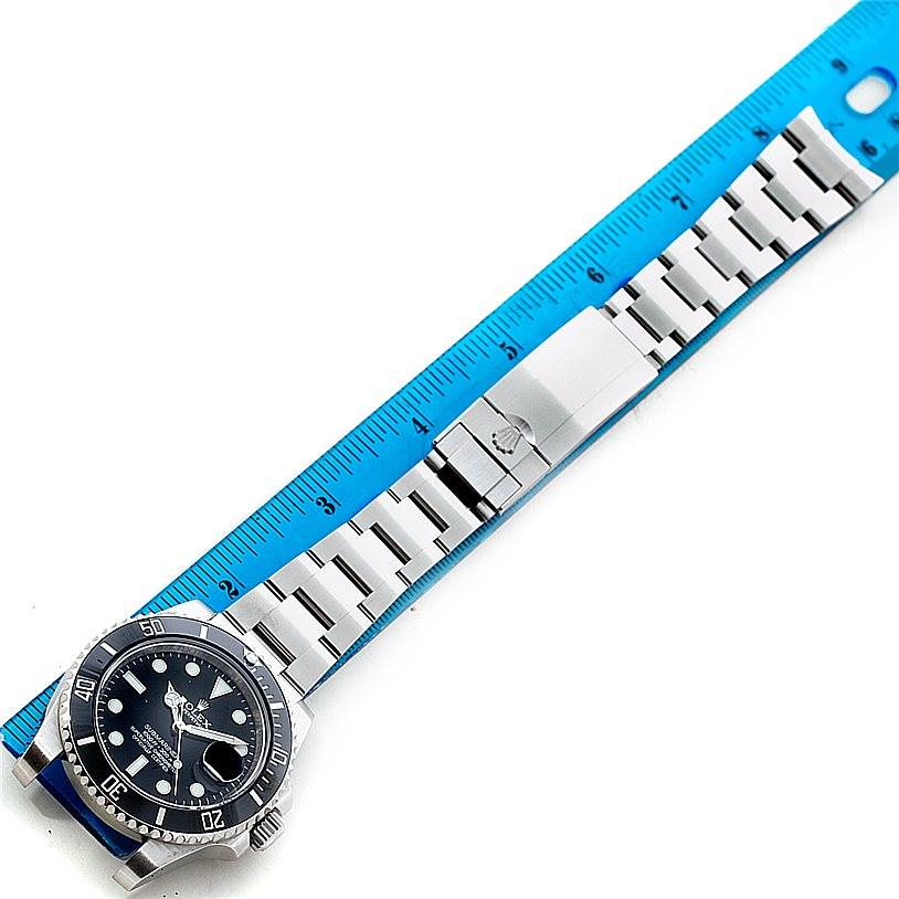 The Rolex Submariner 116610 Men
s Stainless Steel Black Dial 116610 Men
s Stainless Steel Black Dial watch is shown from a top-down angle, highlighting its face, bracelet, and clasp next to a ruler.