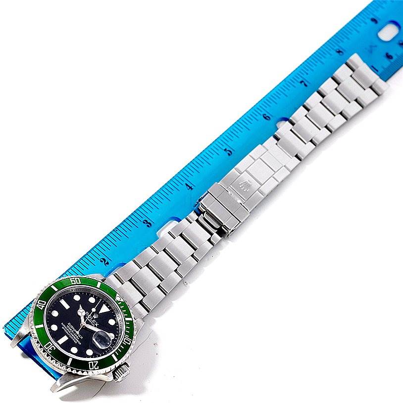 The image shows a top-down view of a Rolex Submariner 16610 Men
s Stainless Steel Black Dial 16610 Men
s Stainless Steel Black Dial watch with its full metal bracelet next to a blue ruler.