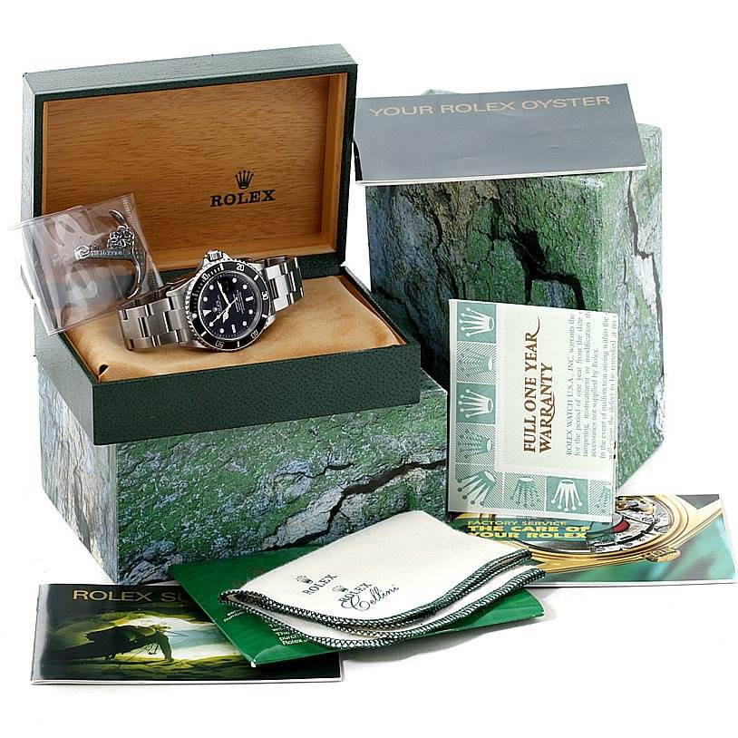 The image shows a Rolex Submariner 16610 Men
s Stainless Steel Black Dial 16610 Men
s Stainless Steel Black Dial within an open box, along with pamphlets, a warranty card, and a cleaning cloth.