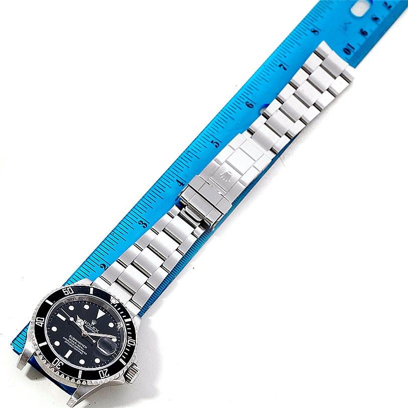 The image shows a Rolex Submariner 16610 Men
s Stainless Steel Black Dial 16610 Men
s Stainless Steel Black Dial watch laid flat alongside a blue ruler, displaying the entire watch and bracelet.
