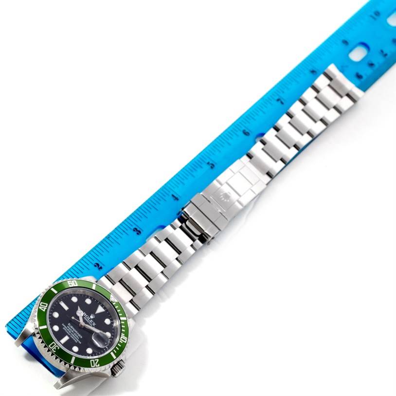 The image shows a Rolex Submariner 16610 Men
s Stainless Steel Black Dial 16610 Men
s Stainless Steel Black Dial watch from a top-down angle, highlighting its green bezel, black dial, and metal bracelet with a deployment clasp.