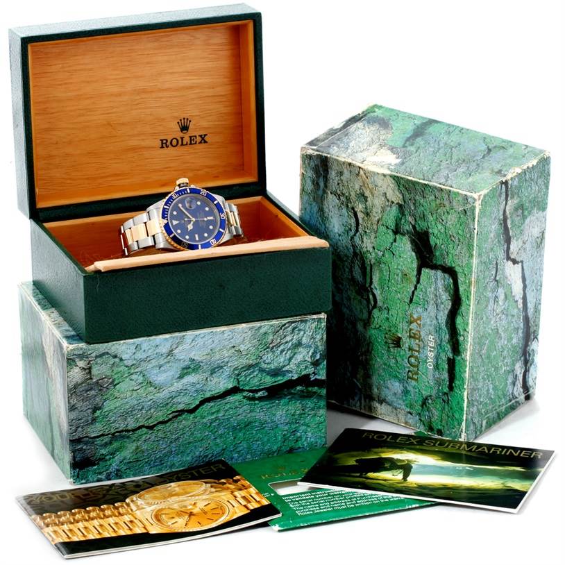 The Rolex Submariner 16613 Men's Steel and Gold (two tone) Blue Dial 16613 Men's Steel and Gold (two tone) Blue Dial watch is shown from the front, placed in an open display box with its packaging and booklets surrounding it.