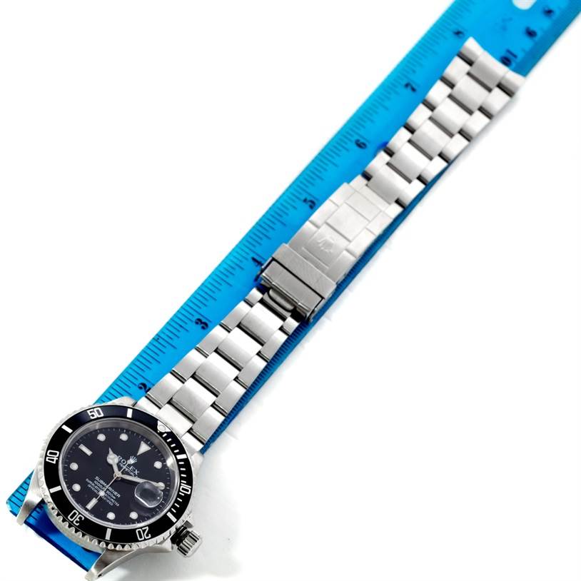 The image shows a top view of a Rolex Submariner 16610 Men
s Stainless Steel Black Dial 16610 Men
s Stainless Steel Black Dial watch with its full bracelet measured against a blue ruler.