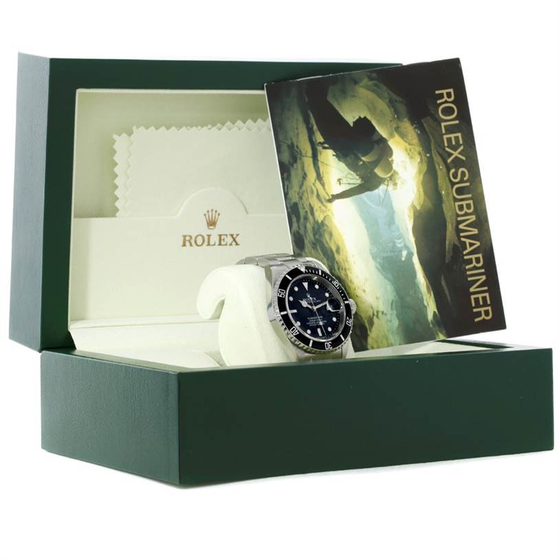The image shows a Rolex Submariner 16610 Men
s Stainless Steel Black Dial 16610 Men
s Stainless Steel Black Dial watch in its box, alongside a booklet and a cleaning cloth, captured from a front angle.