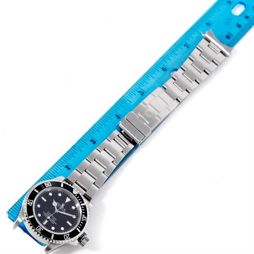 The Rolex Submariner 14060 Men
s Stainless Steel Black Dial 14060 Men
s Stainless Steel Black Dial watch is shown at a slight angle, displaying its face and full stainless steel bracelet alongside a ruler.