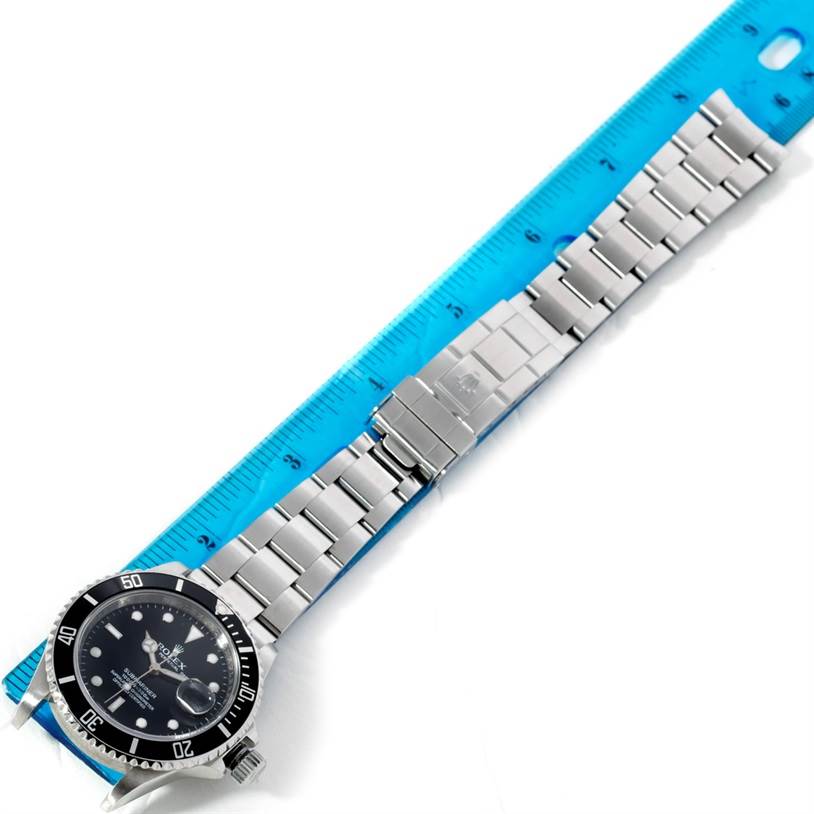 The image shows a top-down view of a Rolex Submariner 16610 Men
s Stainless Steel Black Dial 16610 Men
s Stainless Steel Black Dial watch alongside a ruler, highlighting the watch
s face and metallic bracelet.