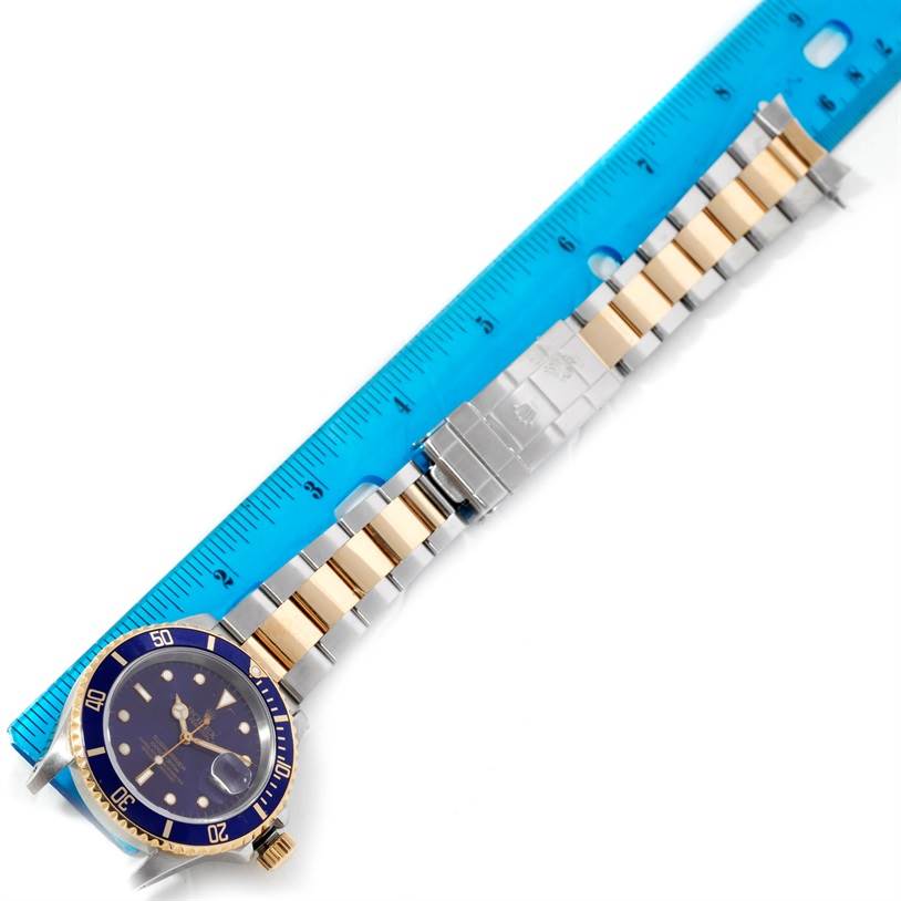 The image shows a full Rolex Submariner 16613 Men's Steel and Gold (two tone) Blue Dial 16613 Men's Steel and Gold (two tone) Blue Dial watch with a blue bezel and dial, laid next to a ruler.