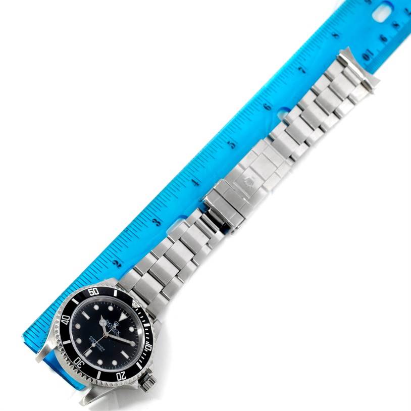 The image shows the Rolex Submariner 14060 Men
s Stainless Steel Black Dial 14060 Men
s Stainless Steel Black Dial watch laid flat with its bracelet extended and measured alongside a blue ruler.